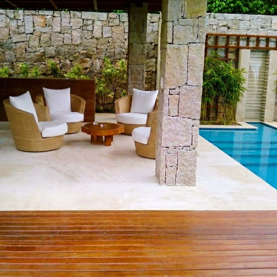 Área externa com piso e coluna em pedra natural ao lado da piscina